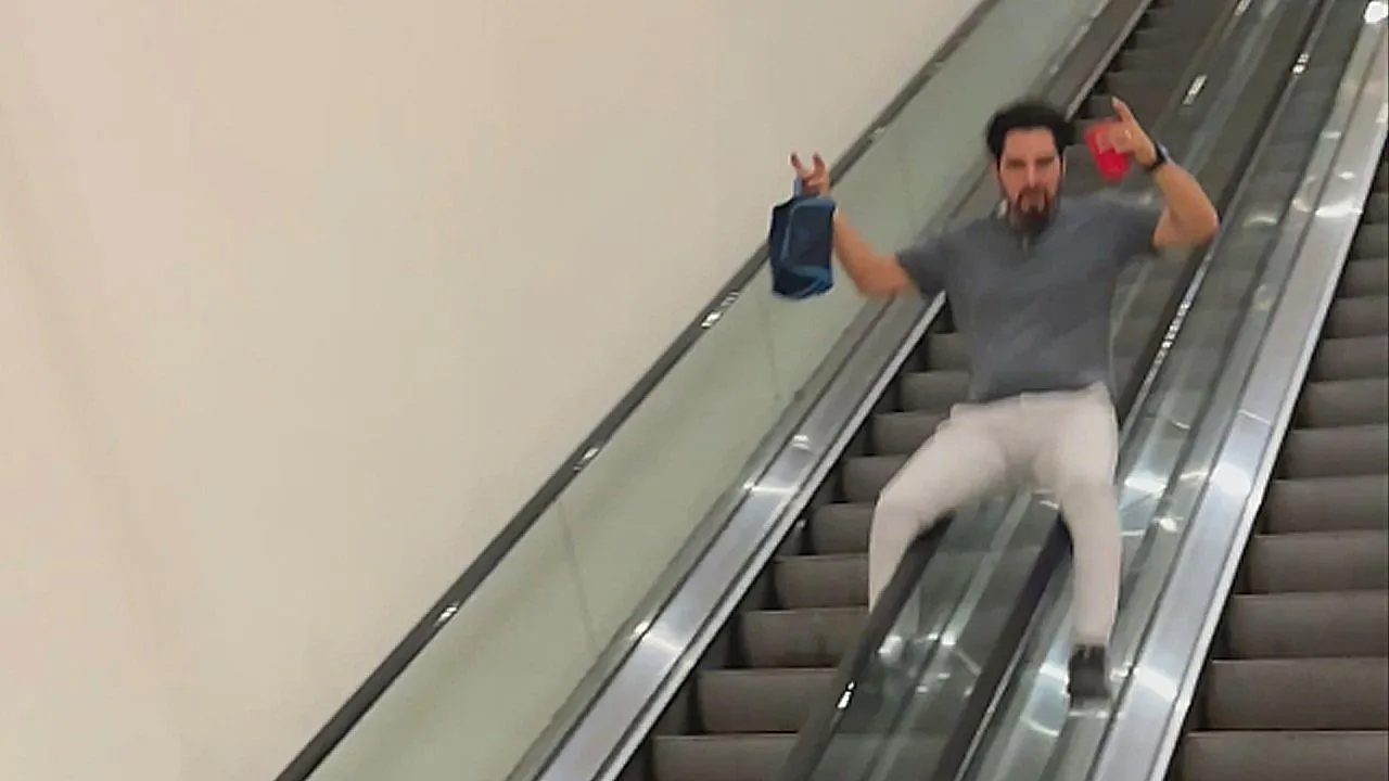 Dronken man glijdt langs gebroken roltrapleuning